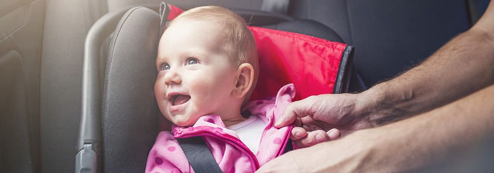 Un père attache son bébé dans un cosy à l'arrière de la voiture