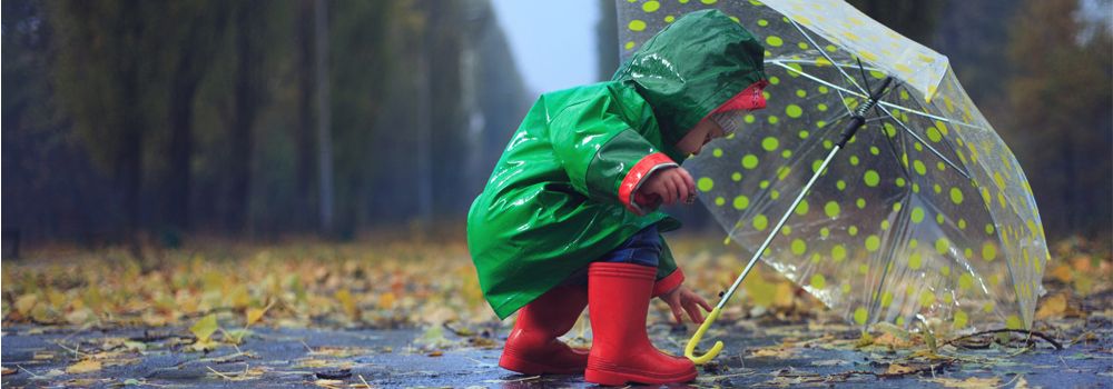 bébé avec imperméable vert, bottes rouges, parapluie transparent