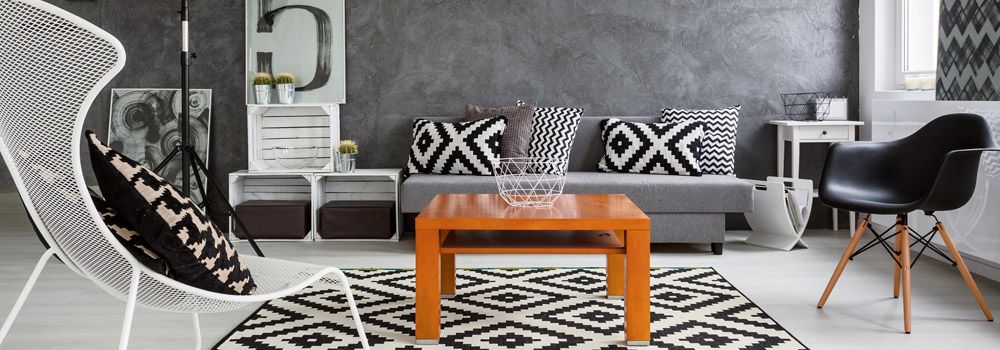 canapé d'angle gris clair, coussins à motifs, tables basses rondes avec pieds métalliques, cadres, plantes